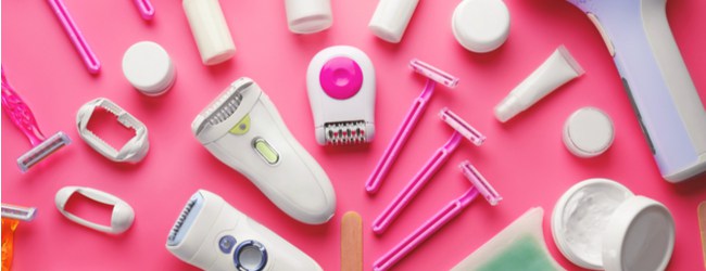 A series of feminine body hair removal products - razors, epilators and so on - arranged on a pink coloured table