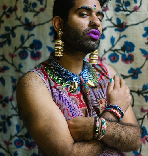 Gender non-conforming poet Alok Vaid Menon. They are dressed in a vibrant sleeveless dress, jewellery and makeup.