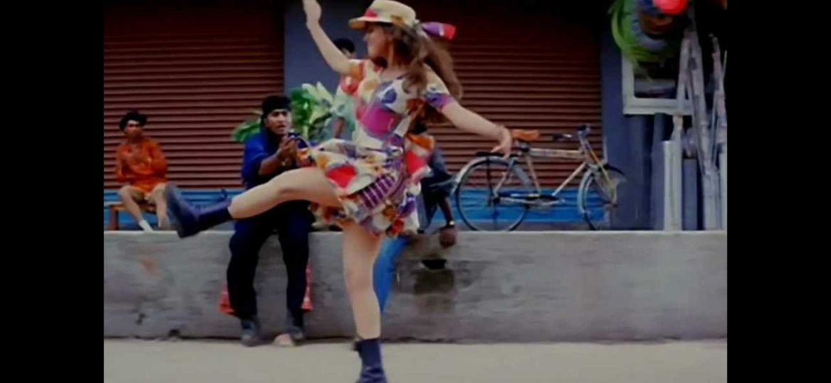 A still from the film Rangeela a girl in a white dress with floral patterns and a hat dances with one leg up
