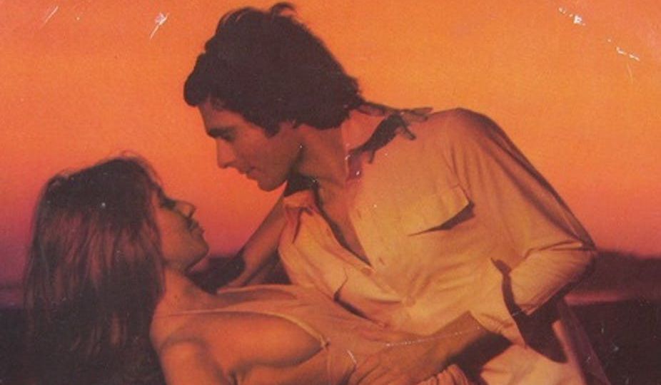 against an orange backdrop, a man leaning down to face a woman, they are in an intimate pose