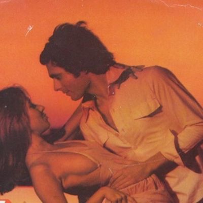 against an orange backdrop, a man leaning down to face a woman, they are in an intimate pose
