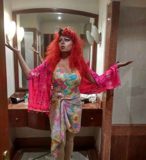A drag queen dressed in a long dress and with a red wig and makeup