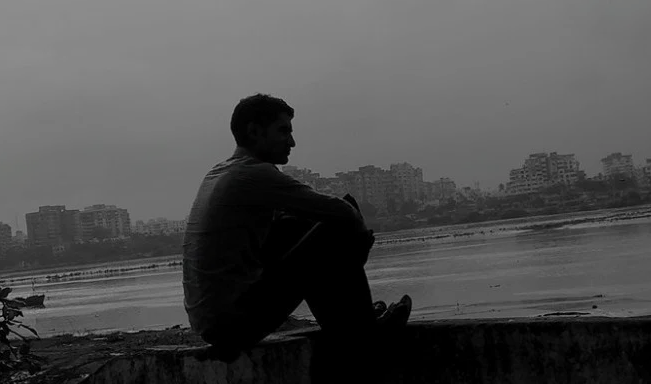 Silhouette of a male figure sitting near a river