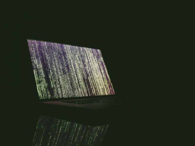 An image of a laptop on a dark background. The screen wallpaper has abstract lines
