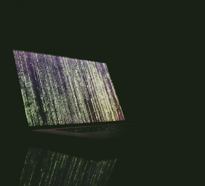 An image of a laptop on a dark background. The screen wallpaper has abstract lines