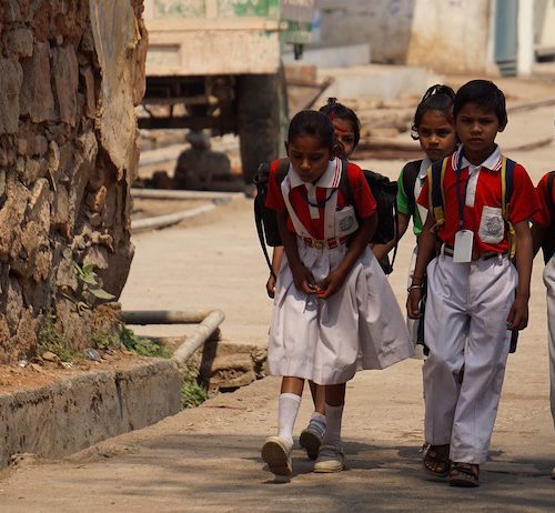 A photograph of young children walking beside a tree clad in red and white school uniform.