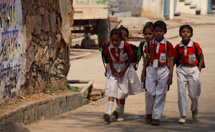 A photograph of young children walking beside a tree clad in red and white school uniform.