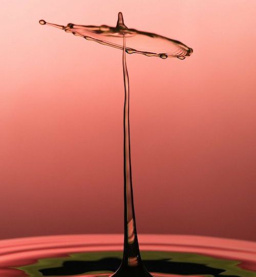 On a pick background, a photograph of a drop of water splashing.