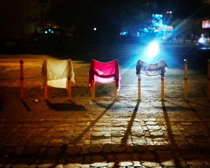A photograph of differently coloured cloths hanging from poles in front of a train station in Mumbai, at night