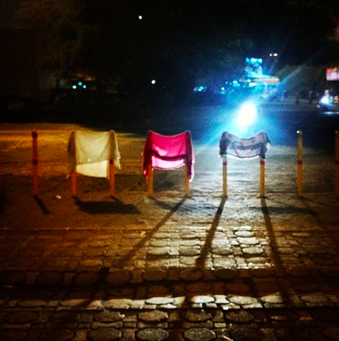 A photograph of differently coloured cloths hanging from poles in front of a train station in Mumbai, at night