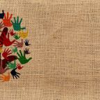 On a jute-textured background, hand-prints in different colours form the leaves of a tree, the trunk and branches of which are a hand-print.