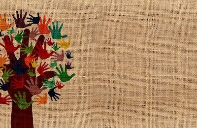 On a jute-textured background, hand-prints in different colours form the leaves of a tree, the trunk and branches of which are a hand-print.