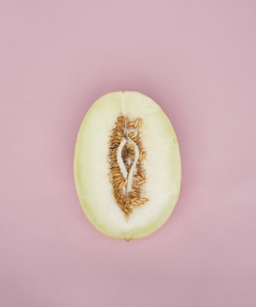 An image of a half cut pear resembling the shape of a vagina. There are seeds around it.