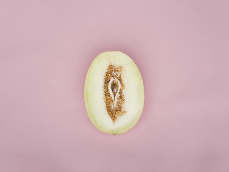 An image of a half cut pear resembling the shape of a vagina. There are seeds around it.