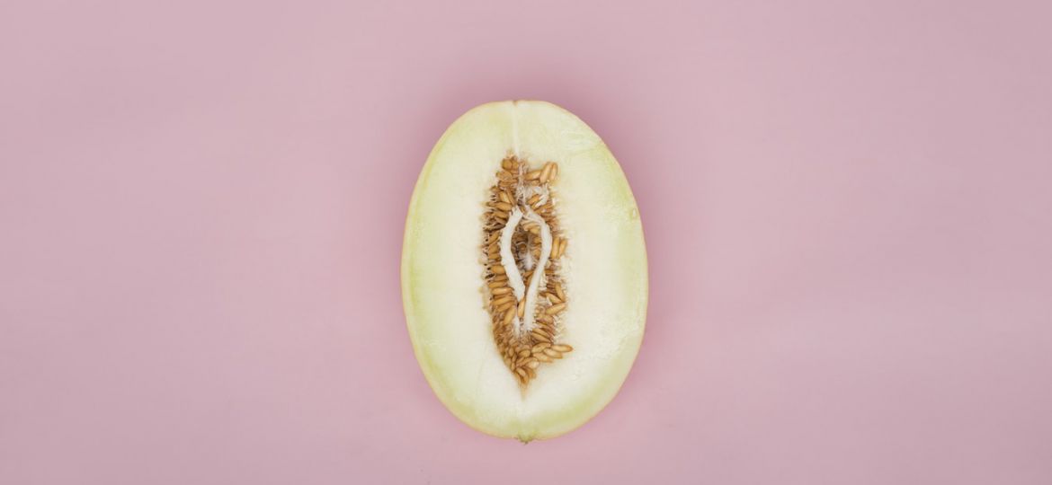 An image of a half cut pear resembling the shape of a vagina. There are seeds around it.