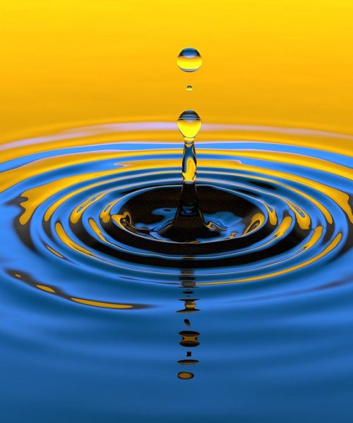 A yellow and blue gradient close-up photograph of a water droplet creating ripples