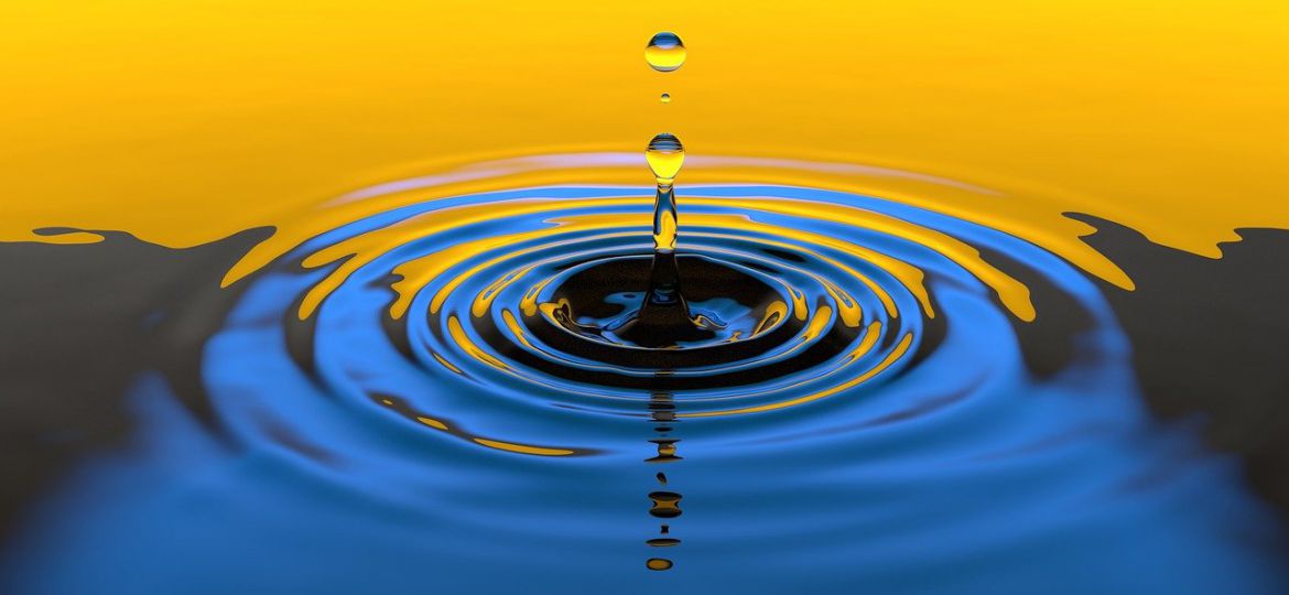 A yellow and blue gradient close-up photograph of a water droplet creating ripples