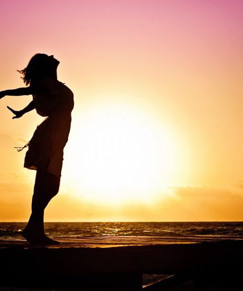 एक लड़की की तस्वीर, जिसमे वह अपने हाथ को पीछे करके और अपना सर ऊपर करके खड़ी है। पीछे समुद्र और ढलता हुआ सूरज दिखाई पड़ रहा है।
