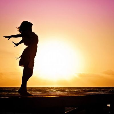 एक लड़की की तस्वीर, जिसमे वह अपने हाथ को पीछे करके और अपना सर ऊपर करके खड़ी है। पीछे समुद्र और ढलता हुआ सूरज दिखाई पड़ रहा है।