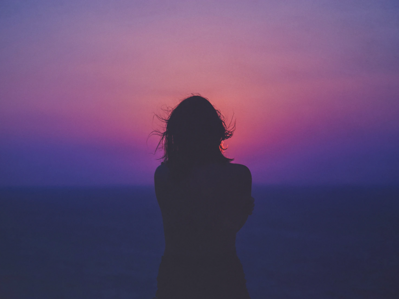 A photograph of a woman’s silhouette against a pink and purple sky.