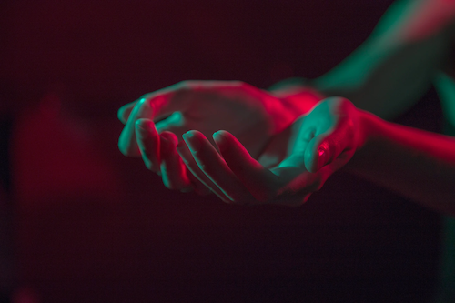 A photograph of a person’s palms held out in prayer. The light is streaked with shades of pink and blue.