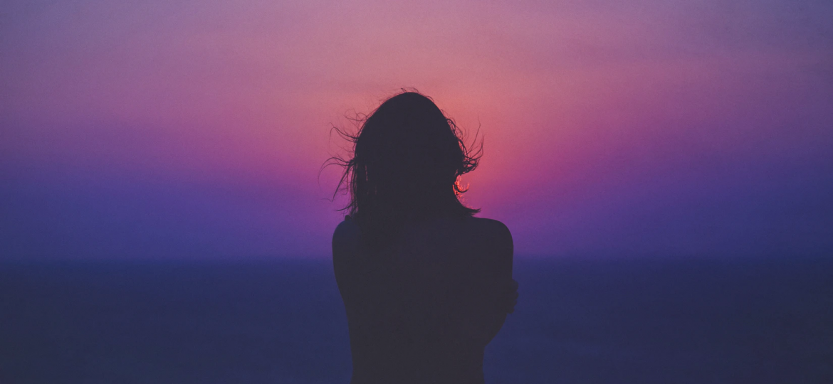 A photograph of a woman’s silhouette against a pink and purple sky.