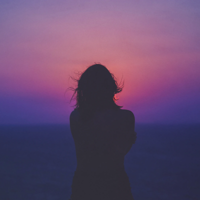 A photograph of a woman’s silhouette against a pink and purple sky.