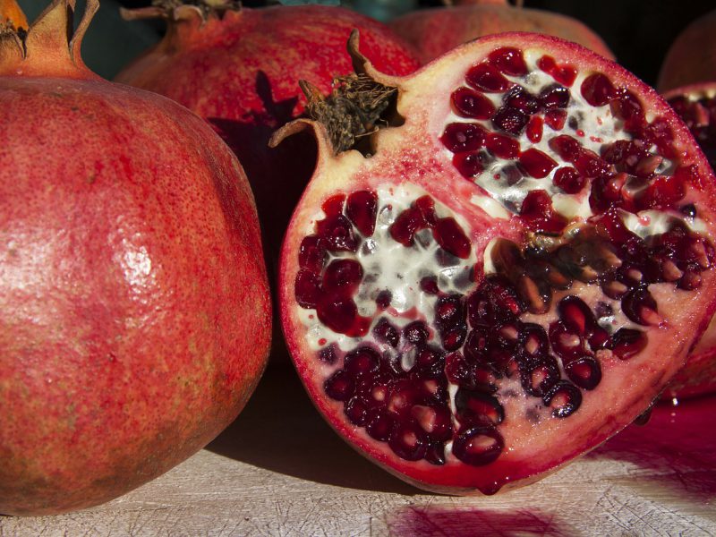 A photograph of pomegranates on a black background, one of them is cut.