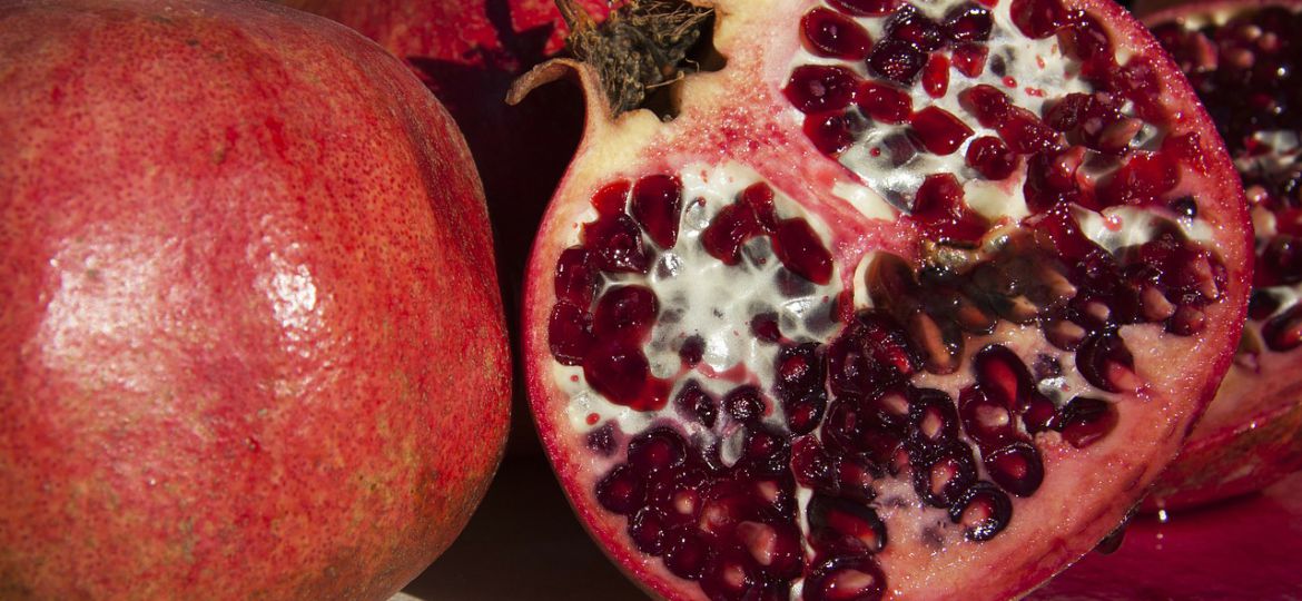 A photograph of pomegranates on a black background, one of them is cut.