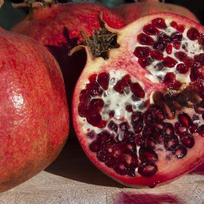 A photograph of pomegranates on a black background, one of them is cut.