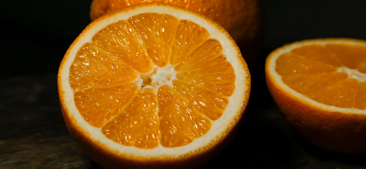 A photograph of oranges on a black background. One orange is whole and the other is halved.