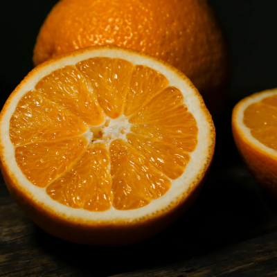 A photograph of oranges on a black background. One orange is whole and the other is halved.