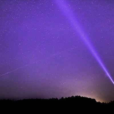 An image of a starry purple sky and a person flashing a white light towards the sky.