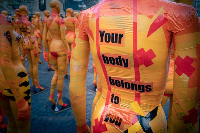 Image of mannequins with orange and pink ductapes. On one of the mannequins ‘Your body belongs to you’ is written