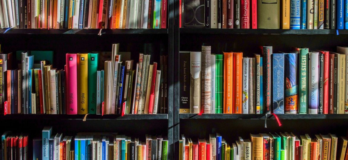 A photograph of a book-shelf, brown-black, with differently coloured books.