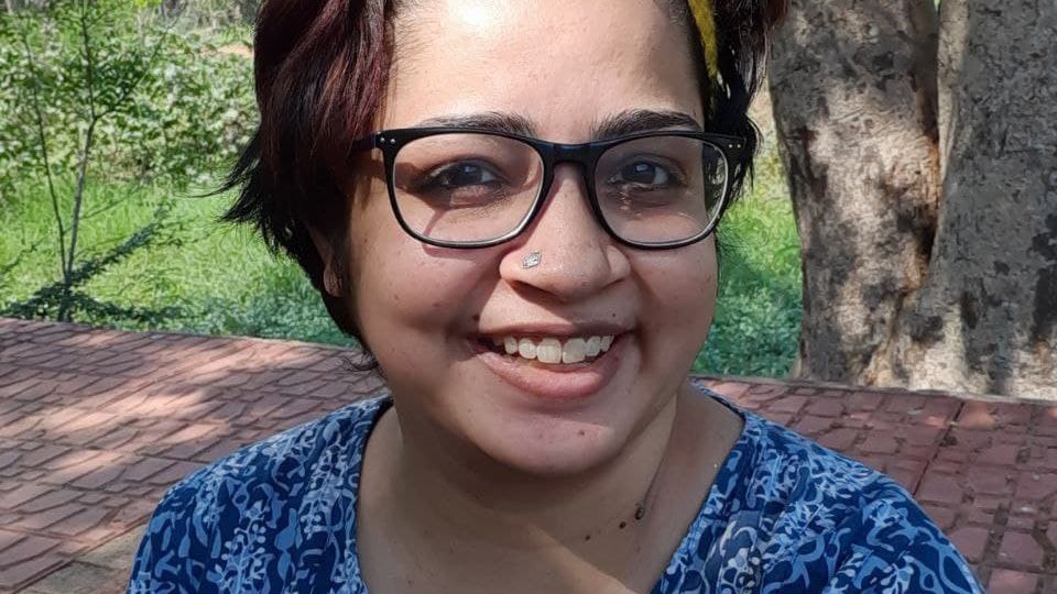 A photograph of disability rights activist Srinidhi Raghavan. She is wearing a blue top with a white pattern, black-rimmed spectacles, and a yellow hair-band.