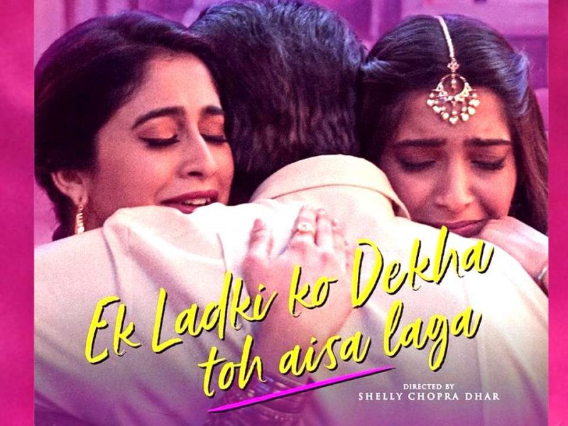 Poster of Bollywood movie ‘Ek Ladki ko Dekha toh aisa laga..’ Two women in traditional Indian attire are hugging a man in a white suit. The women are facing the front, while only the back of the man can be seen. The title of the movie “Ek Ladki ko Dekha toh aisa laga” is written in the bottom center, followed by text that reads “Directed by Shelly Chopra Dhar.”