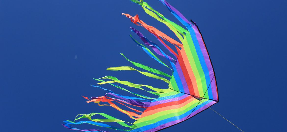 A multi-coloured kite with multiple tails flying against a deep blue sky