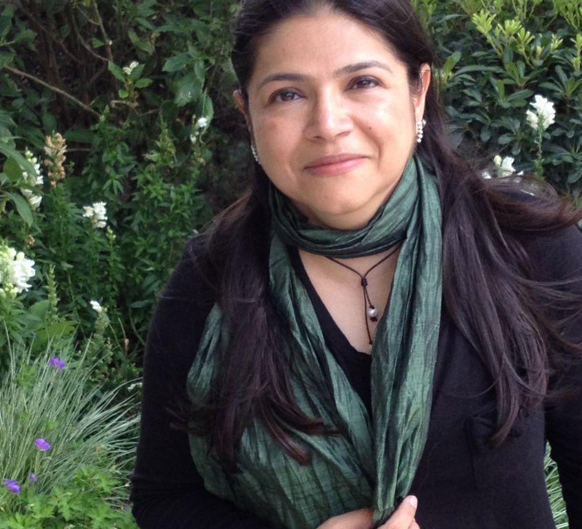 Photo of Sameera Khan. She has long black hair and is standing in a garden. She is wearing a black kurta, a deep emerald dupatta and a black necklace.