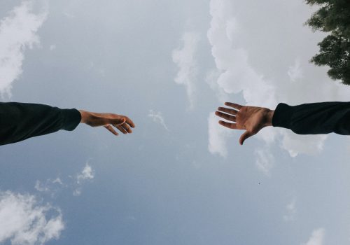 Two hands reaching out to each other against the background of a blue sky.