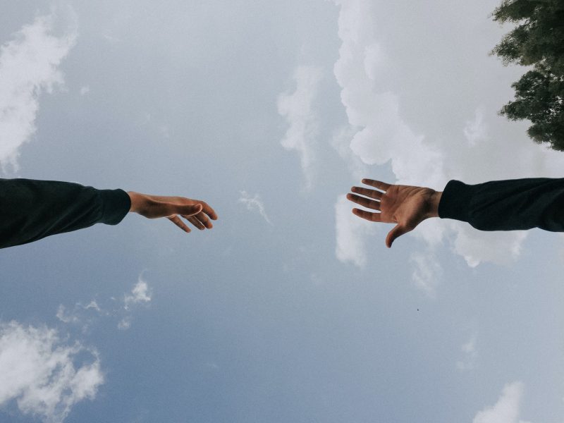 Two hands reaching out to each other against the background of a blue sky.