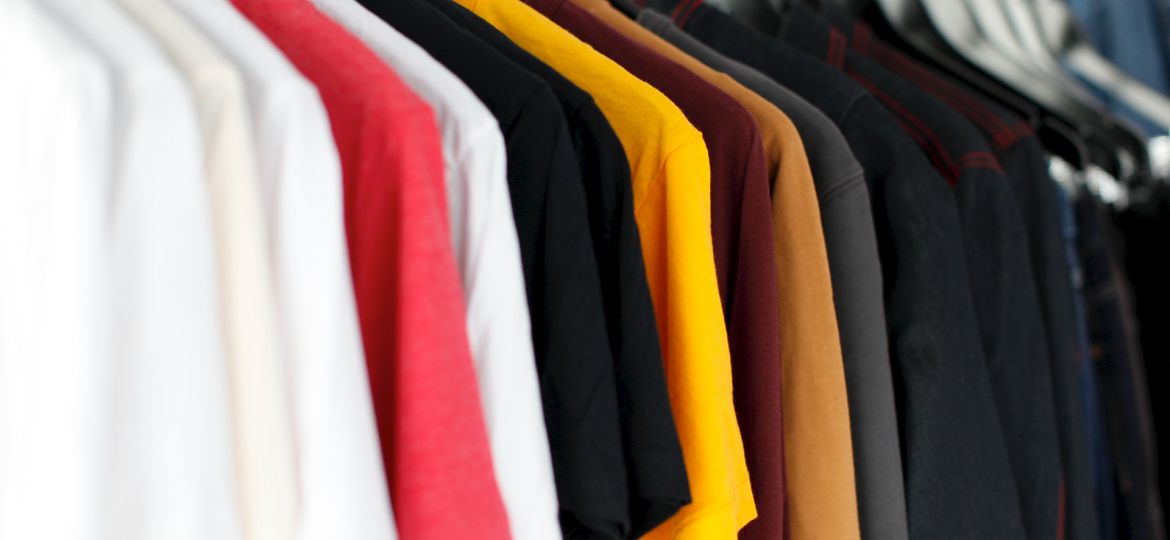 A rack of clothes from where T-shirts of different colours are hanging in a row.