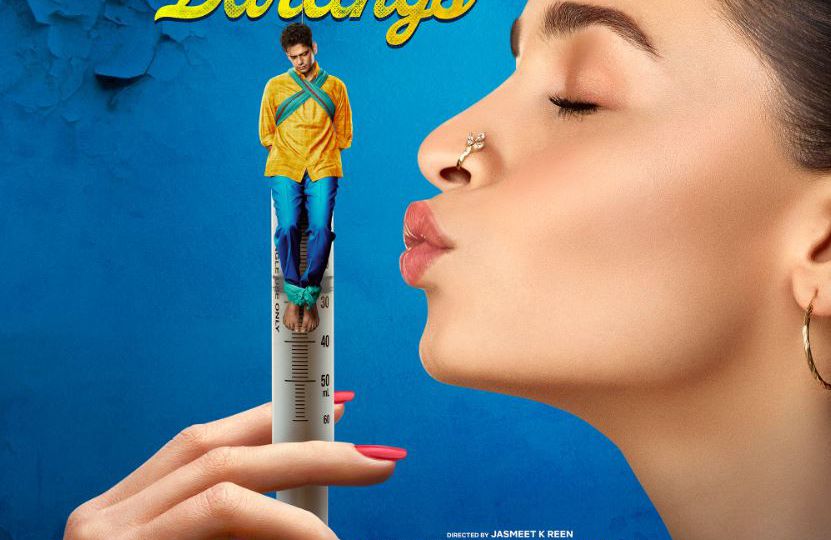 A poster of the movie Darlings. Alia Bhatt is blowing a kiss to a miniature Vijay Varma who is depicted hanging on the top of a syringe.