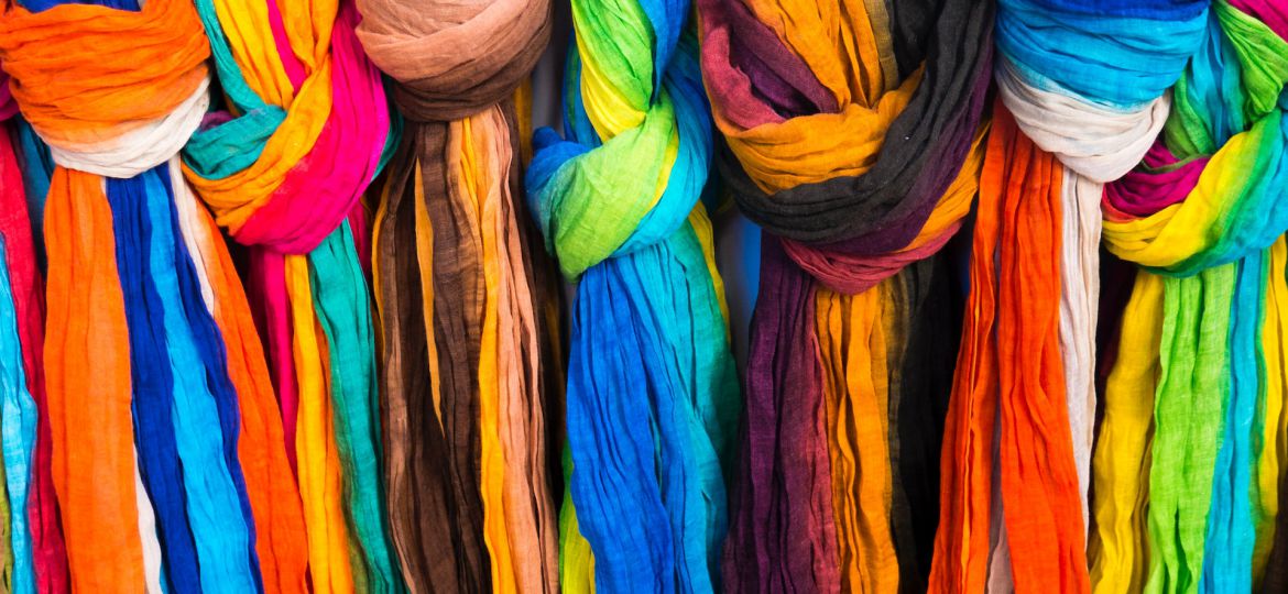 A row Multicoloured scarves or dupattas tied in a knot and hanging from a bar.