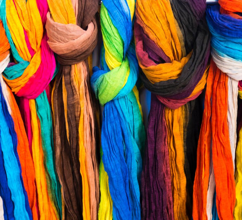 A row Multicoloured scarves or dupattas tied in a knot and hanging from a bar.