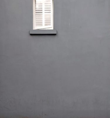 A white window on a grey wall opening up to a cobblestone street