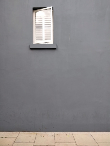 A white window on a grey wall opening up to a cobblestone street