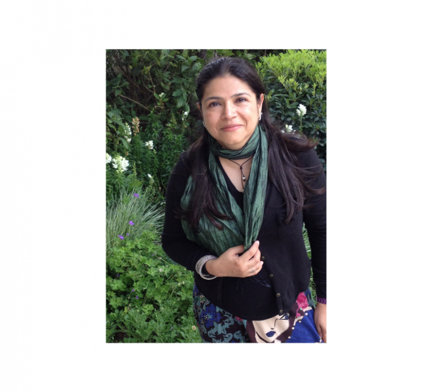 Photo of Sameera Khan. She has long black hair and is standing in a garden. She is wearing a black kurta, a deep emerald dupatta and a black necklace.