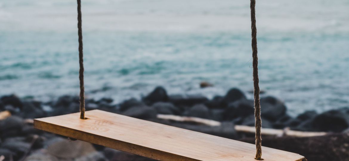 A brown wooden swing chair beside shoreline.