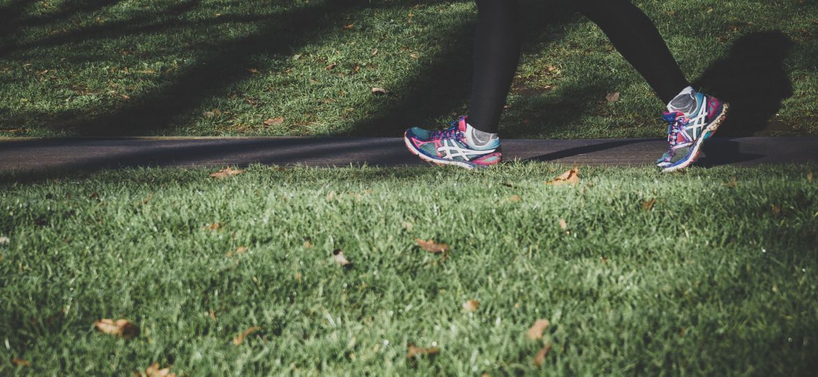 A close-up of a person walking on a path in a park. They are on the right side of the photo and only their legs are visible.